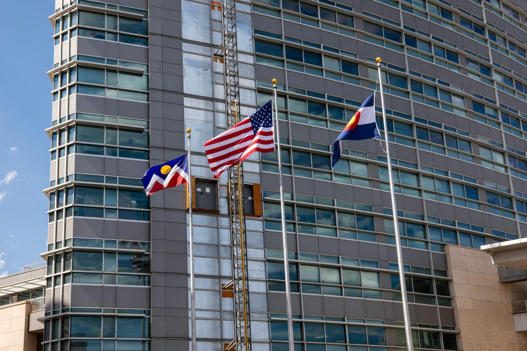 Colorado flags in front of a modern high-rise building under a blue sky
